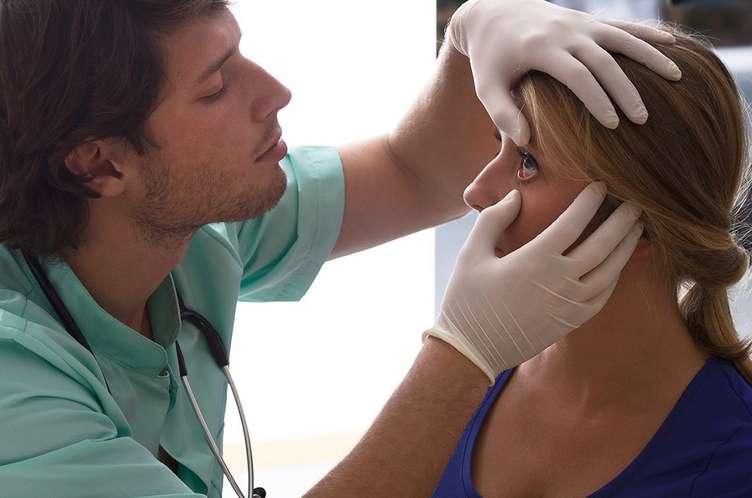 Image of an eye doctor checking a woman's eye. He is wearing latex gloves.