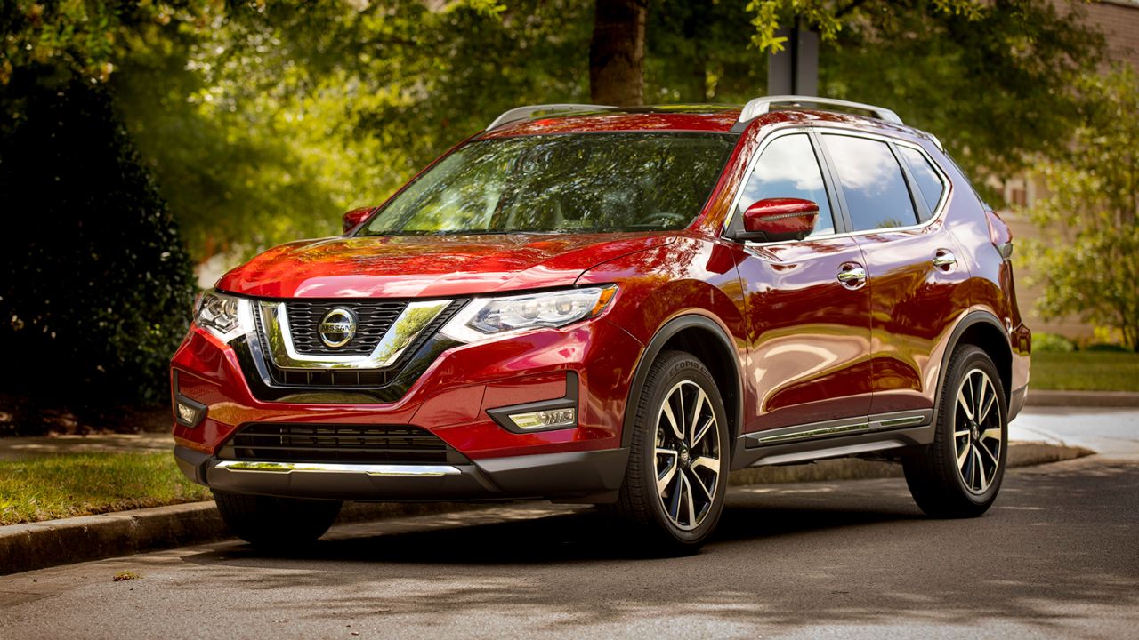 Red Nissan Rogue, parked on a street. There are green trees in the background.
